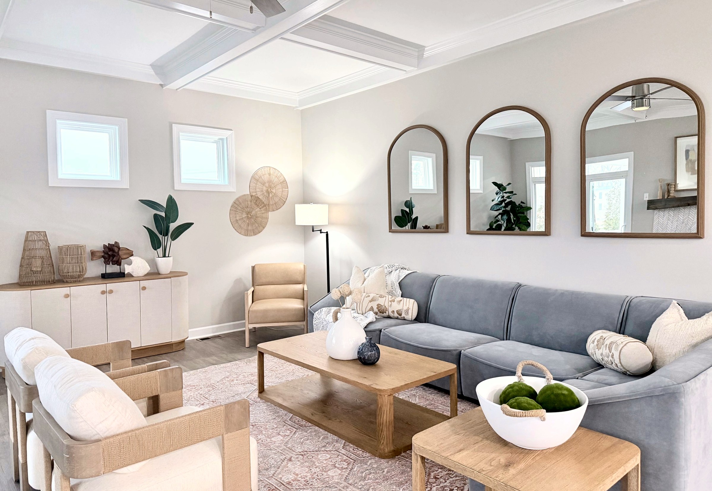 Staged living room with a soft blue sectional, three arched mirrors, and natural wood accents